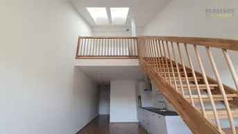 Heller offener Wohnbereich mit kleiner Küchenzeile, Holztreppe und Dachfenstern.