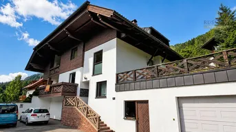 Alpines Wohnhaus mit weißer Fassade, Holzelementen und Balkonen in sonniger Berglandschaft.