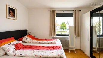 Schlafzimmer mit Doppelbett, Parkettboden und Fenster mit Blick ins Grüne und auf ein Gebäude.