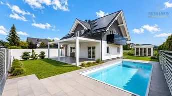 Modernes Einfamilienhaus mit Garten, privatem Pool und Photovoltaikanlage unter blauem Himmel.