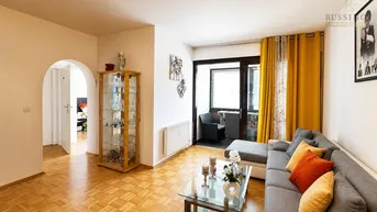 Helles Wohnzimmer mit Parkettboden, gemütlichem Sofa und Zugang zu einem kleinen Balkon.