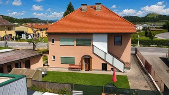 Hausfassade mit rotem Ziegeldach, kleinem Vorgarten und Blick auf die ländliche Umgebung.