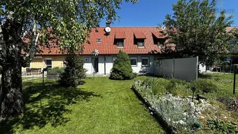 Gepflegter Gartenbereich hinter dem Haus mit Rasenfläche, Blumenbeeten und Blick auf die Rückseite des Gebäudes.
