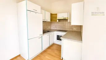 Helle Einbauküche mit weißen Schränken, integrierten Geräten und Laminatboden.