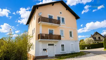 Klassisches Mehrfamilienhaus mit zwei Balkonen und heller Fassade unter blauem Himmel.