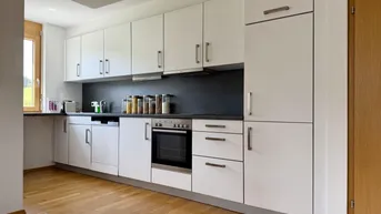 Moderne Einbauküche mit weißen Schränken, dunkler Arbeitsplatte und Holzboden.