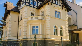 Historische Villa mit eleganter Fassade, Fachwerkdetails und gepflegtem Vorgarten unter blauem Himmel.