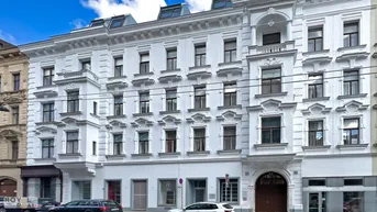 Klassisches Altbaugebäude mit weißer Fassade, vielen Fenstern und Balkonen in städtischer Umgebung.