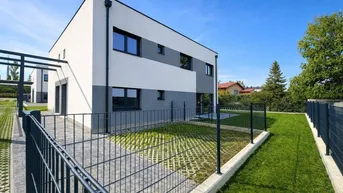 Modernes Reihenhaus mit weiß-grauer Fassade, gepflegtem Rasen und gepflastertem Zugangsbereich.