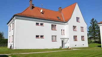 Weißes Wohngebäude mit rotem Ziegeldach und gepflegtem Vorgarten unter blauem Himmel.