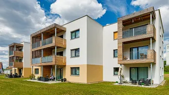 Moderne Wohngebäude mit weißer und beiger Fassade, ausgestattet mit Holz-Balkonen und Terrassen mit direktem Zugang zum Garten.