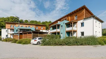 Moderne Wohngebäude mit Holzfassaden und Balkonen in grüner Umgebung und Parkplätzen.