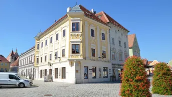 Historisches Gebäude mit gelber Fassade und roten Dächern an einem sonnigen Platz.