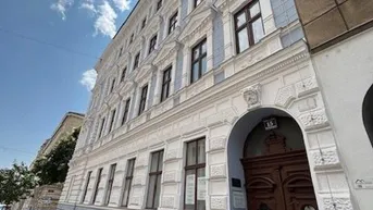 Historische Fassade eines Altbaus mit eleganten Details und blauen Akzenten unter blauem Himmel.