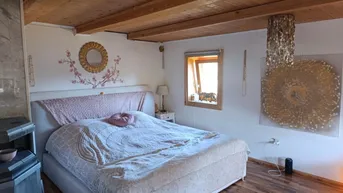 Schlafzimmer mit Holzbalkendecke, großem Bett und einem Kaminofen, der eine gemütliche Atmosphäre schafft.
