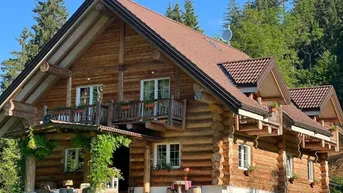 Charmantes Blockhaus mit Holzbalkonen und Satteldach, umgeben von grünen Bäumen und Natur.