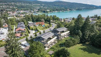 Luftaufnahme von modernen Wohngebäuden mit Flachdach und Seeblick in grüner Umgebung.