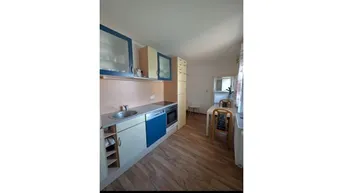 Funktionale Küche mit blauen und beigen Schränken, Laminatboden und Essbereich.