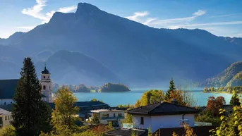 Panoramablick auf einen malerischen See, umgeben von majestätischen Bergen und herbstlicher Vegetation.