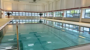 Großes Hallenbad mit natürlichem Lichteinfall und Blick ins Grüne, ideal für Sport und Entspannung.