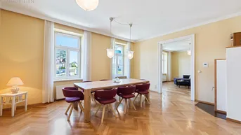 Geräumiges Esszimmer mit Fischgrätparkett, hohen Fenstern und Zugang zu einem weiteren Raum.