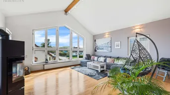 Helles Wohnzimmer mit hohen Decken, Holzbalken, Kaminofen und großen Fenstern mit Weitblick.