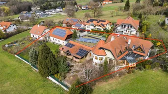 Luftaufnahme eines weitläufigen Anwesens mit mehreren Gebäuden, umgeben von grünen Hügeln und mit Solaranlagen auf den Dächern.