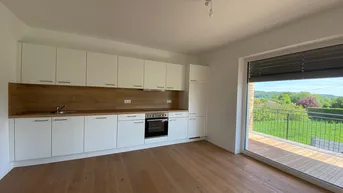 Moderne Einbauküche mit weißen Schränken, Holzarbeitsplatte und Zugang zu einem Balkon mit grüner Aussicht.