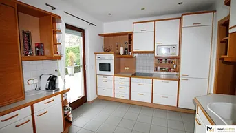 Funktionale Küche mit Holzschränken, weißen Fronten, Einbaugeräten und Zugang zum Garten.