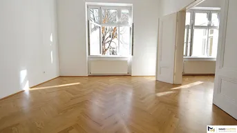 Helles Zimmer mit Fischgrätparkettboden und großen Fenstern, das viel Tageslicht hereinlässt.