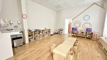 Geräumiger Spielraum mit Holzboden, Kindermöbeln und Wickelbereich, ideal für eine Kindertagesstätte.