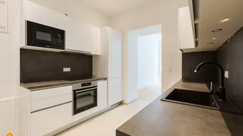 Moderne Küche mit weißen Hochglanzfronten, dunkler Arbeitsplatte und integrierten Geräten.