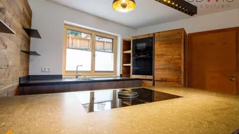 Moderne Küche mit dunklen Arbeitsplatten, Holzelementen und integrierten Geräten.