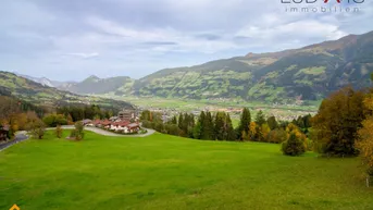 Weitläufige grüne Landschaft mit sanften Hügeln und einem Dorf im Tal, umgeben von Bergen.