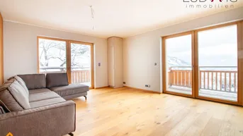 Helles Wohnzimmer mit modernem Sofa, Holzboden und Zugang zu einem Balkon mit Bergblick.