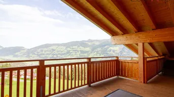 Großer Holzbalkon mit weitem Blick auf die umliegende Berglandschaft und grüne Täler.