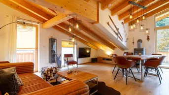 Gemütlicher Wohn-Essbereich im Dachgeschoss mit Holzbalken, Kaminofen und Zugang zum Balkon.