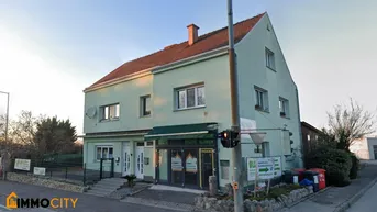 Gebäude mit hellgrüner Fassade und rotem Ziegeldach an einer Straßenecke mit Geschäft im Erdgeschoss.