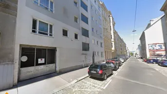 Gebäudeansicht von der Straße mit parkenden Autos und der Einfahrt zur Tiefgarage.