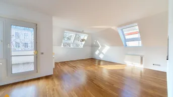 Helles Dachgeschosszimmer mit Holzboden, Dachfenstern und Zugang zu einem kleinen Balkon.