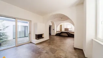 Geräumiges Wohnzimmer mit modernem Kamin, Fliesenboden und Zugang zu einem kleinen Innenhof.
