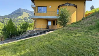 Gelbes Wohnhaus in Hanglage mit moderner Architektur und grüner Umgebung, umgeben von Bergen.