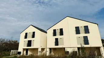 Zwei moderne Neubauhäuser mit heller Fassade und schwarzen Dächern in einer ruhigen Umgebung.