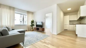 Helles Wohnzimmer mit Parkettboden, Sofa und offener Küchenzeile in modernem Stil.