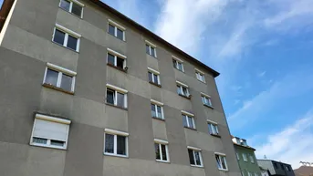 Fassade eines Mehrfamilienhauses mit zahlreichen Fenstern und Rollläden unter blauem Himmel.