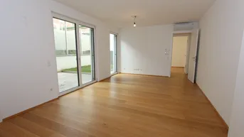 Heller, leerer Wohnraum mit Holzboden und großen Schiebetüren zum Außenbereich.