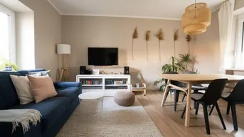 Helles Wohn- und Esszimmer mit modernem Sofa, Esstisch und Holzboden, durchflutet von Tageslicht.