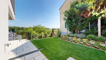 Gepflegter Gartenbereich mit Rasenfläche, gepflasterter Terrasse und Blick ins Grüne.