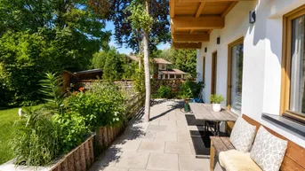 Sonniger Terrassenbereich mit Holzbänken und üppiger Bepflanzung, ideal zum Entspannen im Freien.