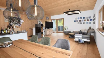 Geräumiger offener Wohn- und Essbereich mit Holzboden, Kaminofen und modernen Pendelleuchten.